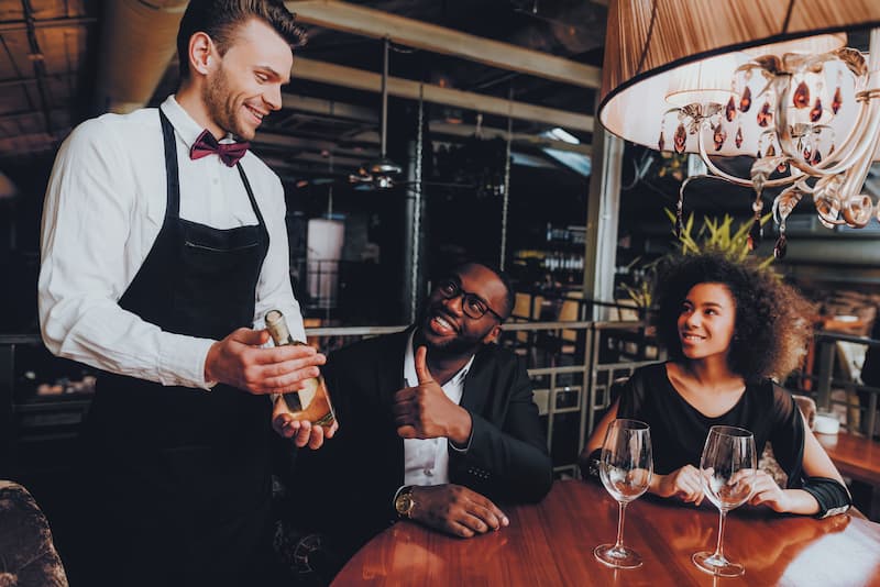 A staff member enthusiastically presenting a bottle of wine to guests